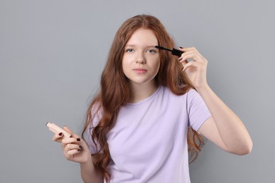 Teenage girl applying mascara on light grey background