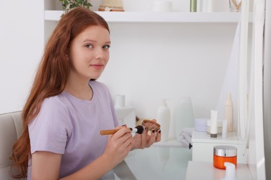 Teenage girl applying blush with brush near mirror indoors