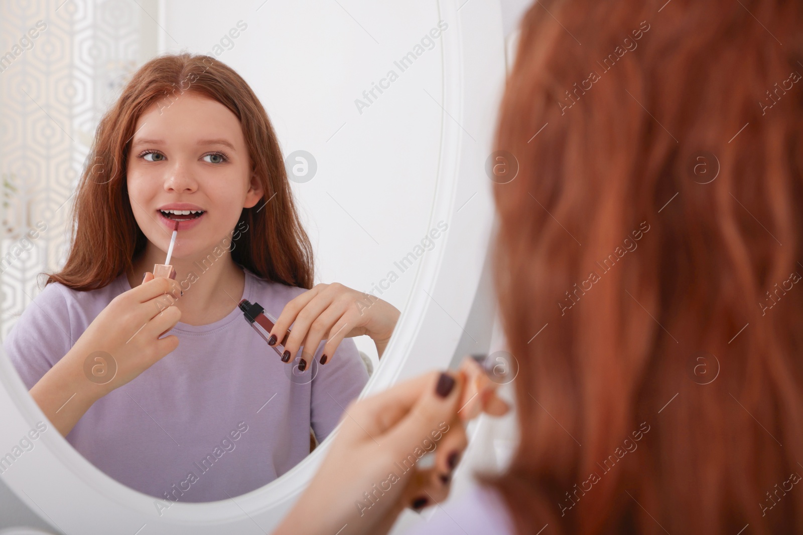 Photo of Teenage girl applying lipgloss near mirror indoors