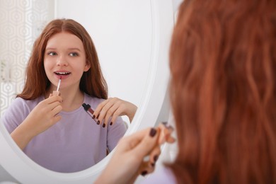 Teenage girl applying lipgloss near mirror indoors