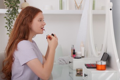 Photo of Teenage girl applying lipgloss near mirror indoors