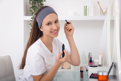 Teenage girl applying mascara near mirror indoors