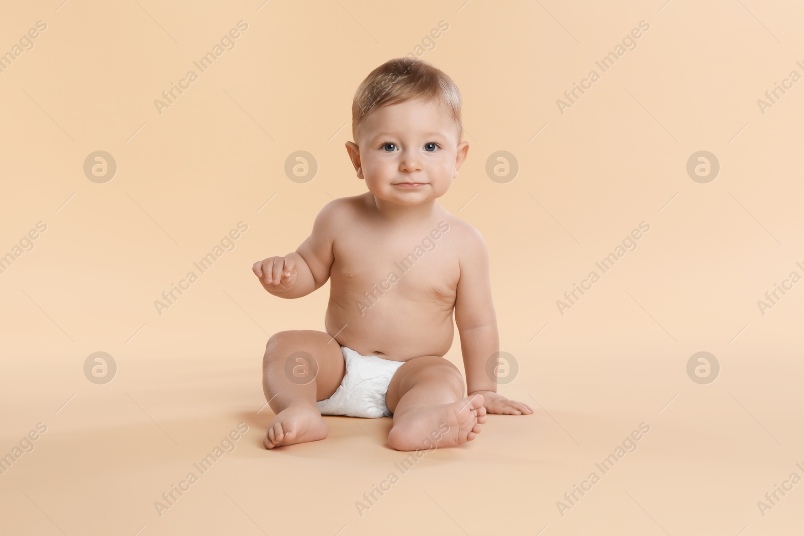 Photo of Cute little baby in diaper sitting on beige background