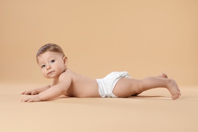 Photo of Cute little baby in diaper crawling on beige background