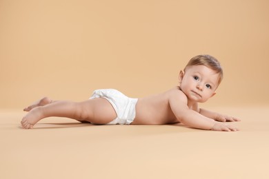 Photo of Cute little baby in diaper crawling on beige background