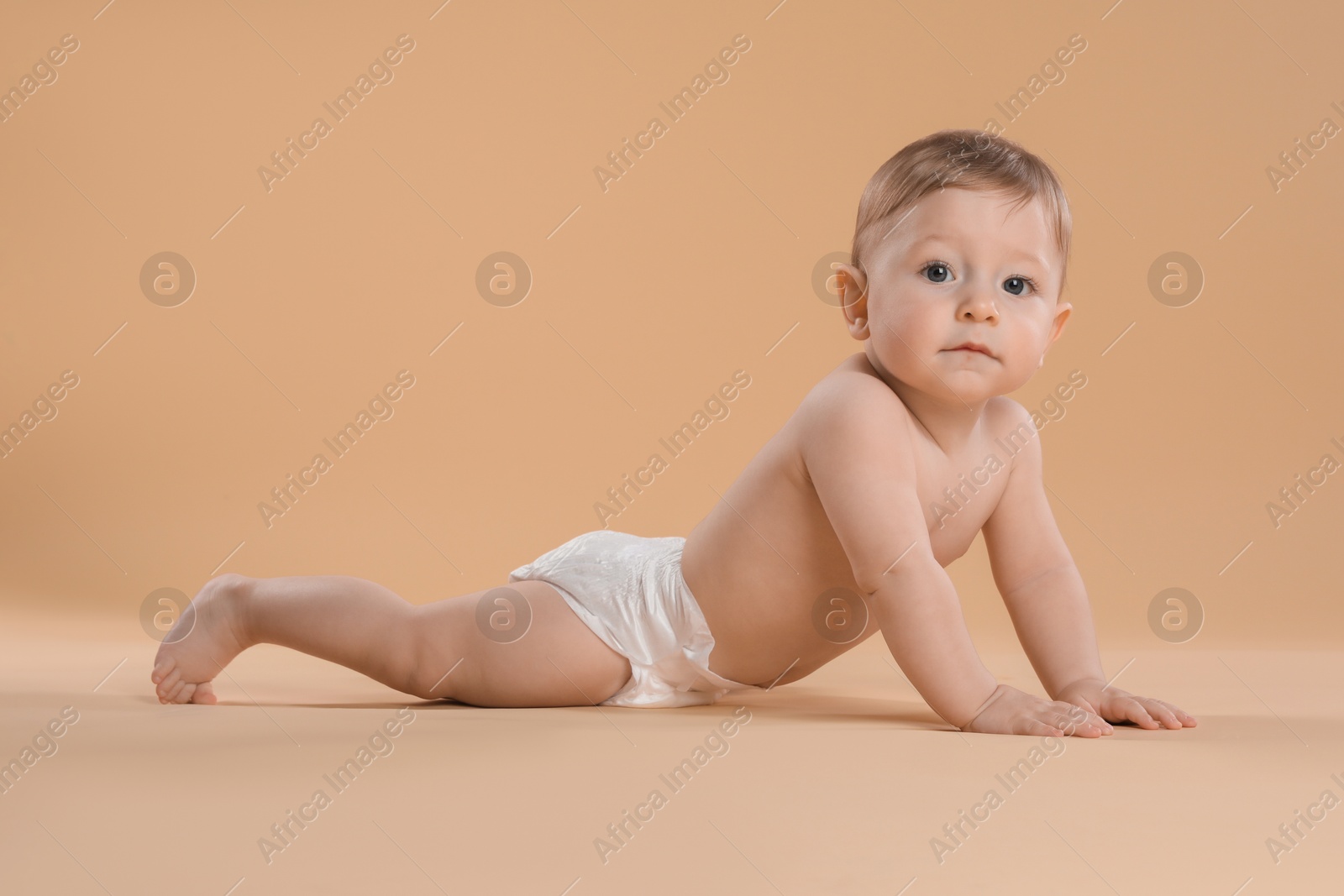 Photo of Cute little baby in diaper crawling on beige background