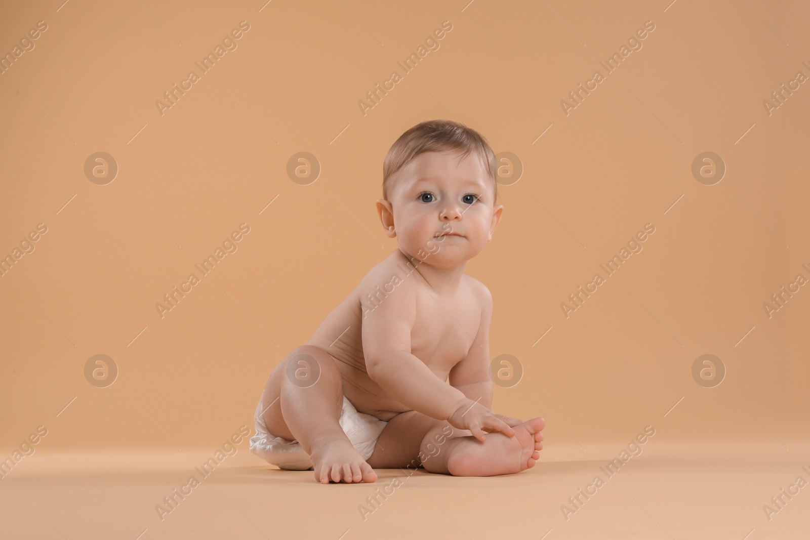 Photo of Cute little baby in diaper sitting on beige background