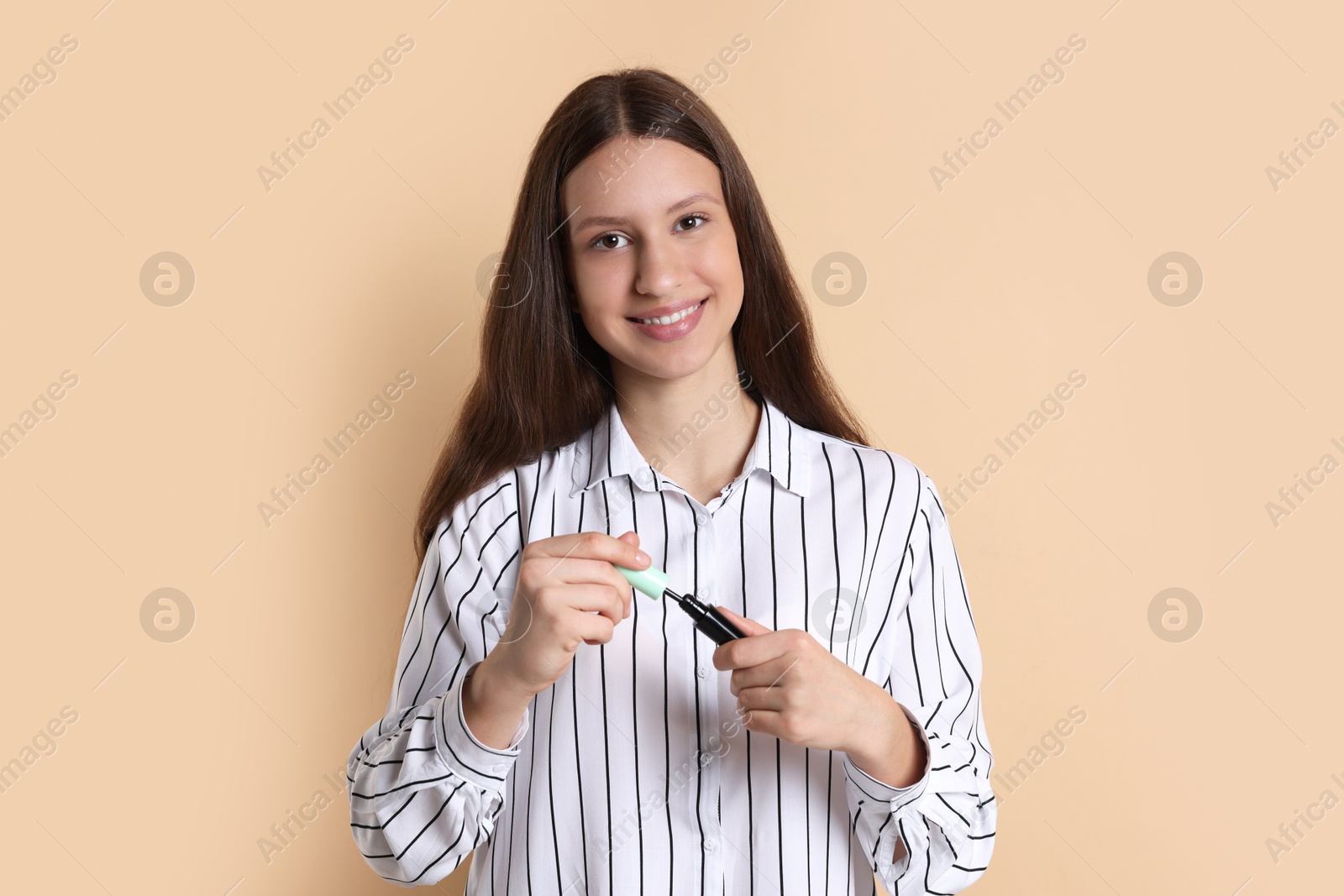 Photo of Smiling teenage girl applying mascara on beige background