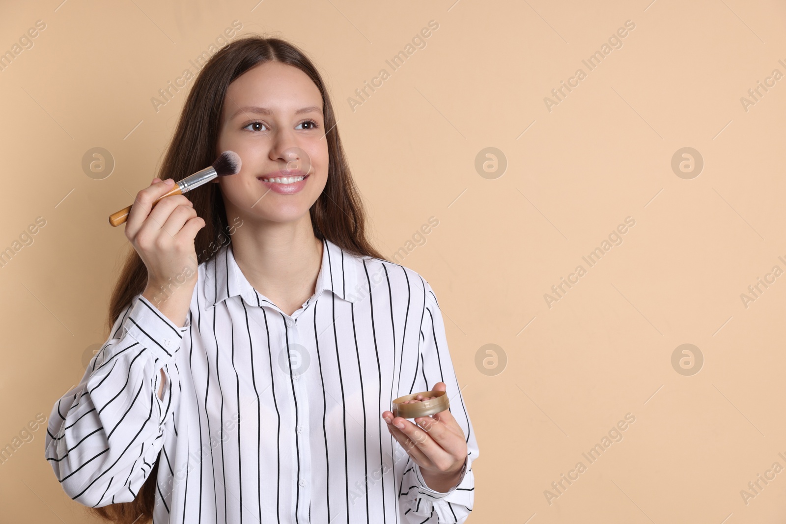 Photo of Smiling teenage girl applying blusher on beige background. Space for text