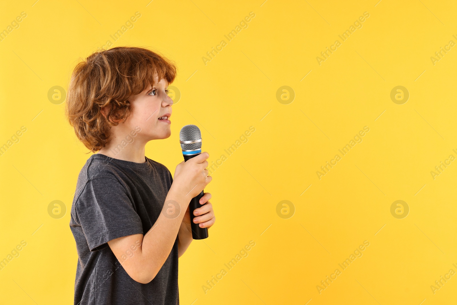 Photo of Little boy with microphone singing on yellow background, space for text