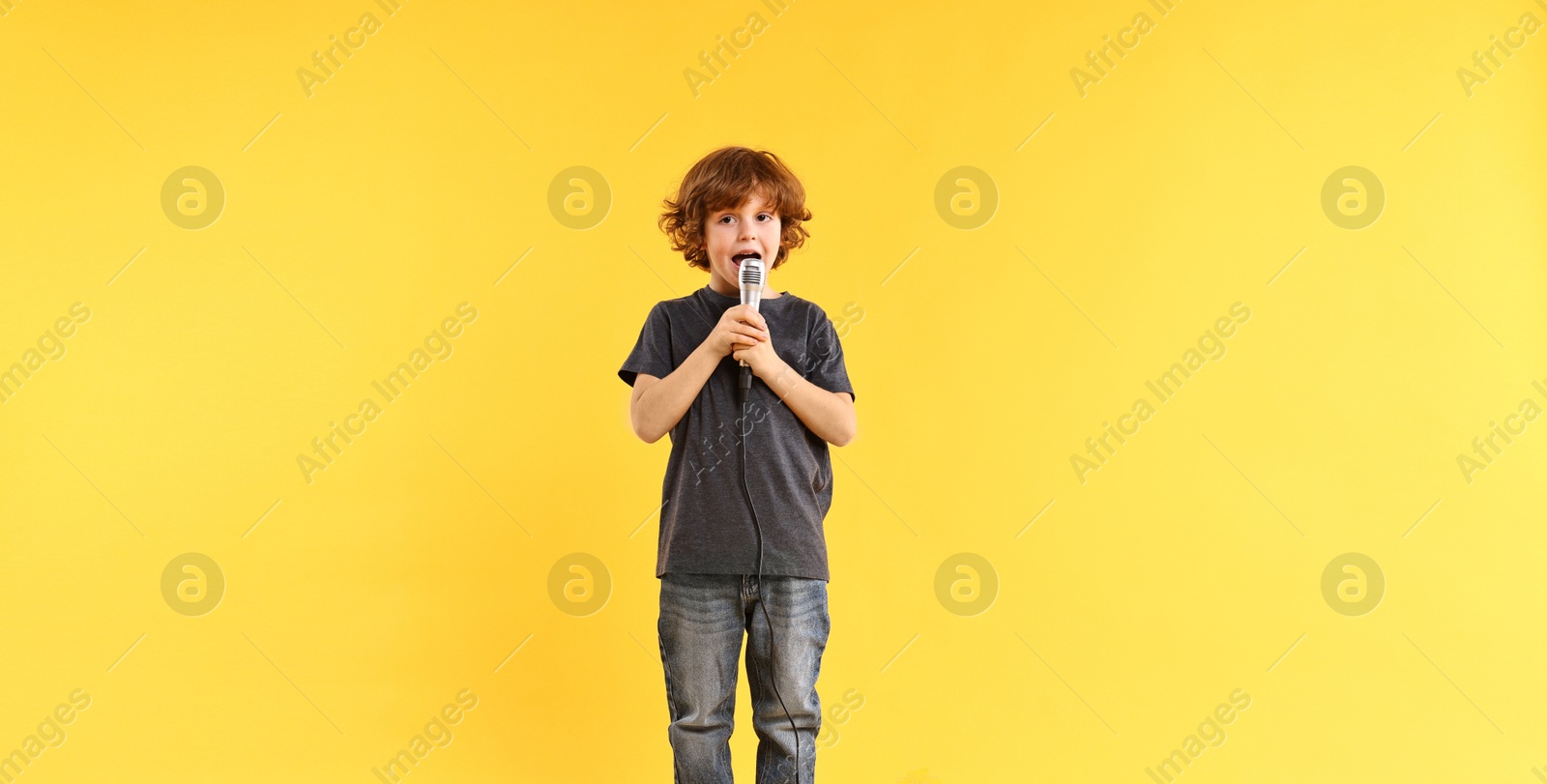 Photo of Little boy with microphone singing on yellow background