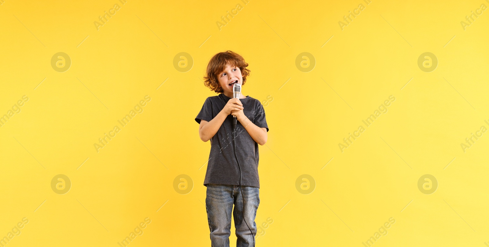 Photo of Little boy with microphone singing on yellow background