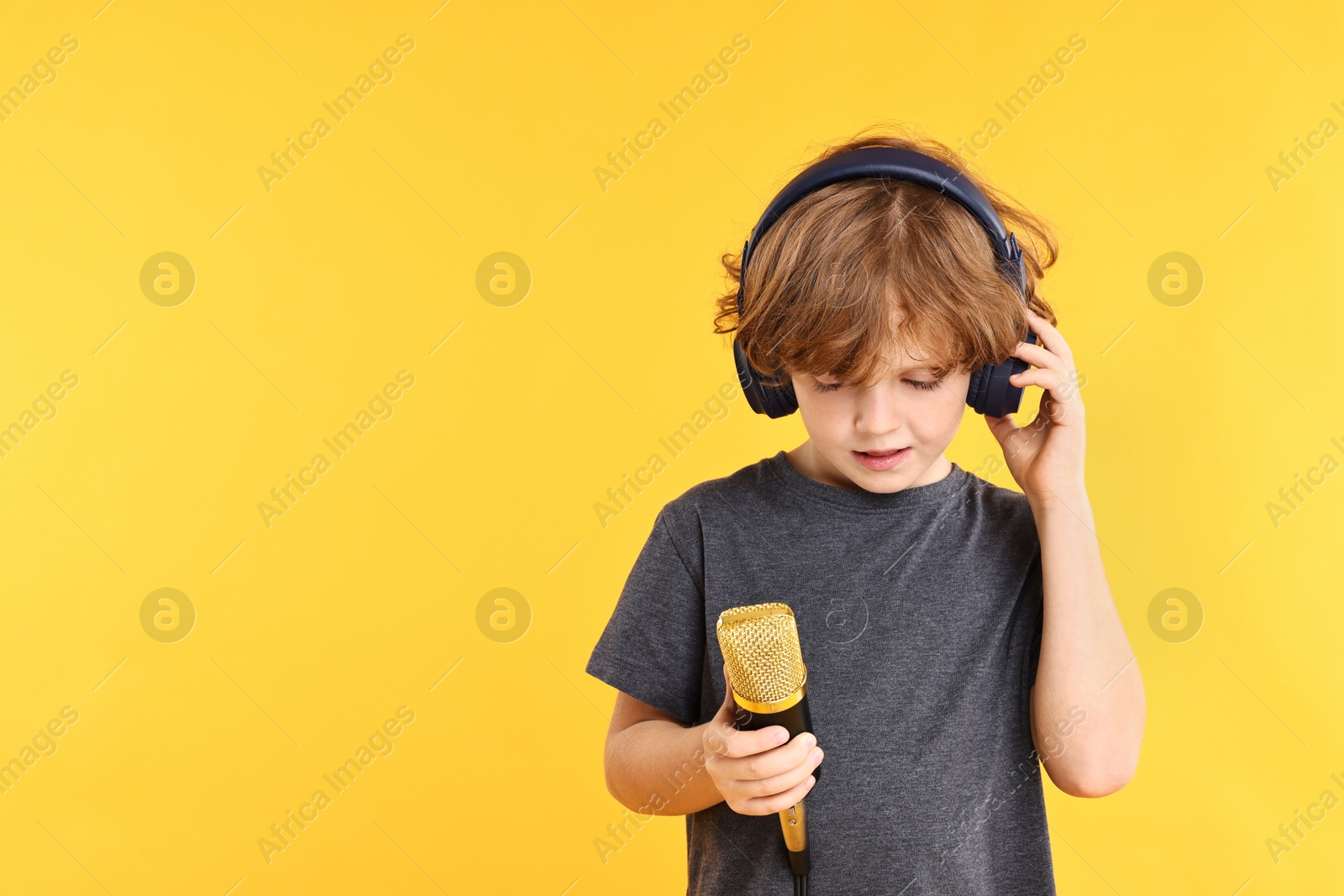 Photo of Little boy with microphone and headphones on yellow background, space for text