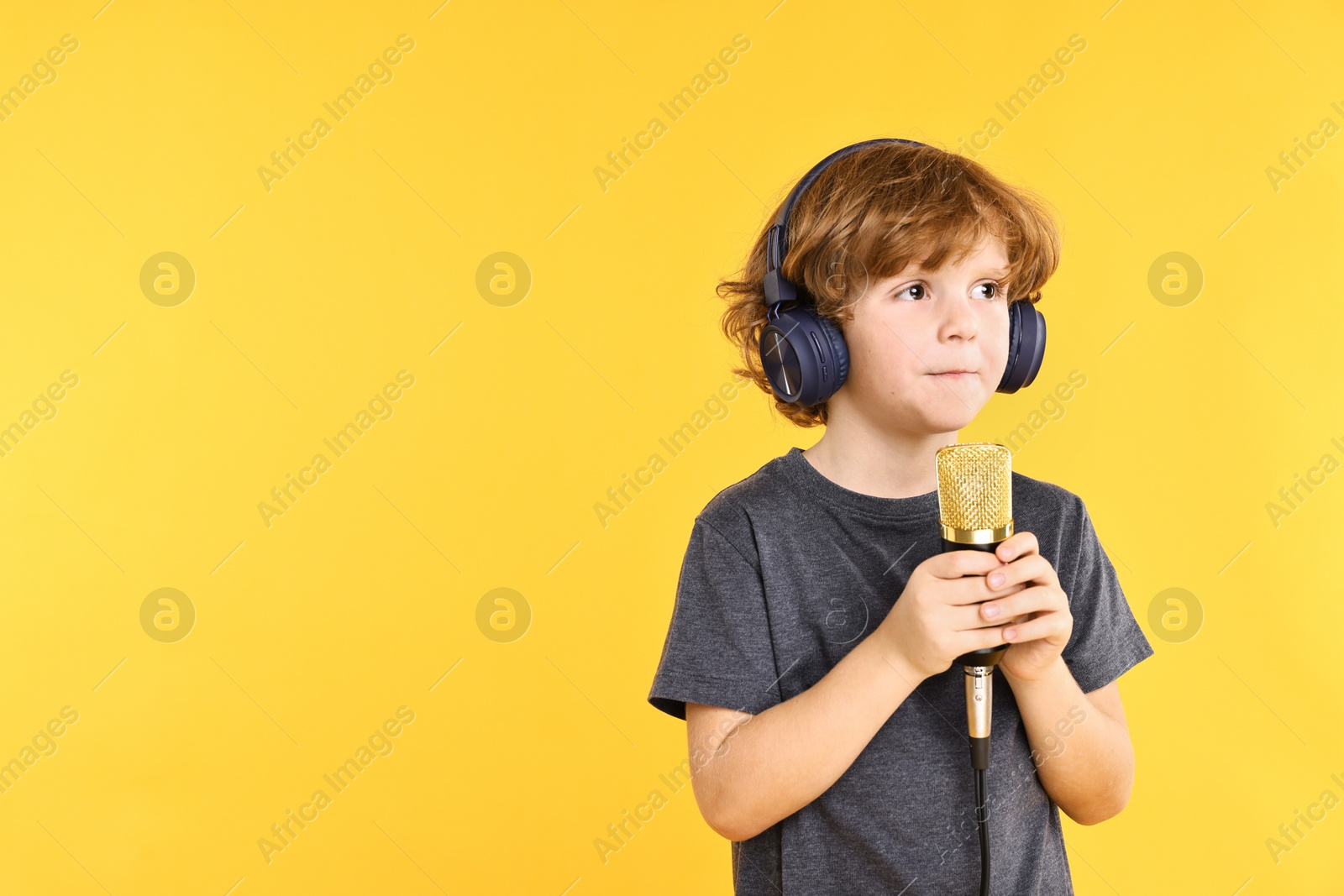 Photo of Little boy with microphone and headphones on yellow background, space for text