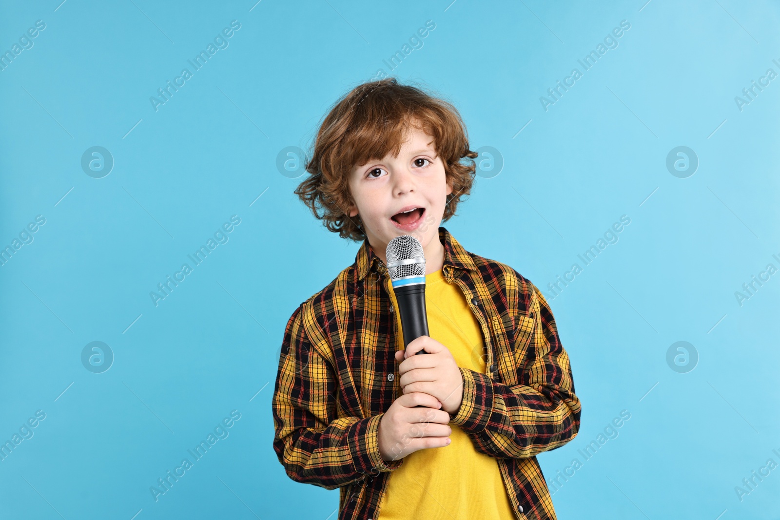 Photo of Little boy with microphone on light blue background