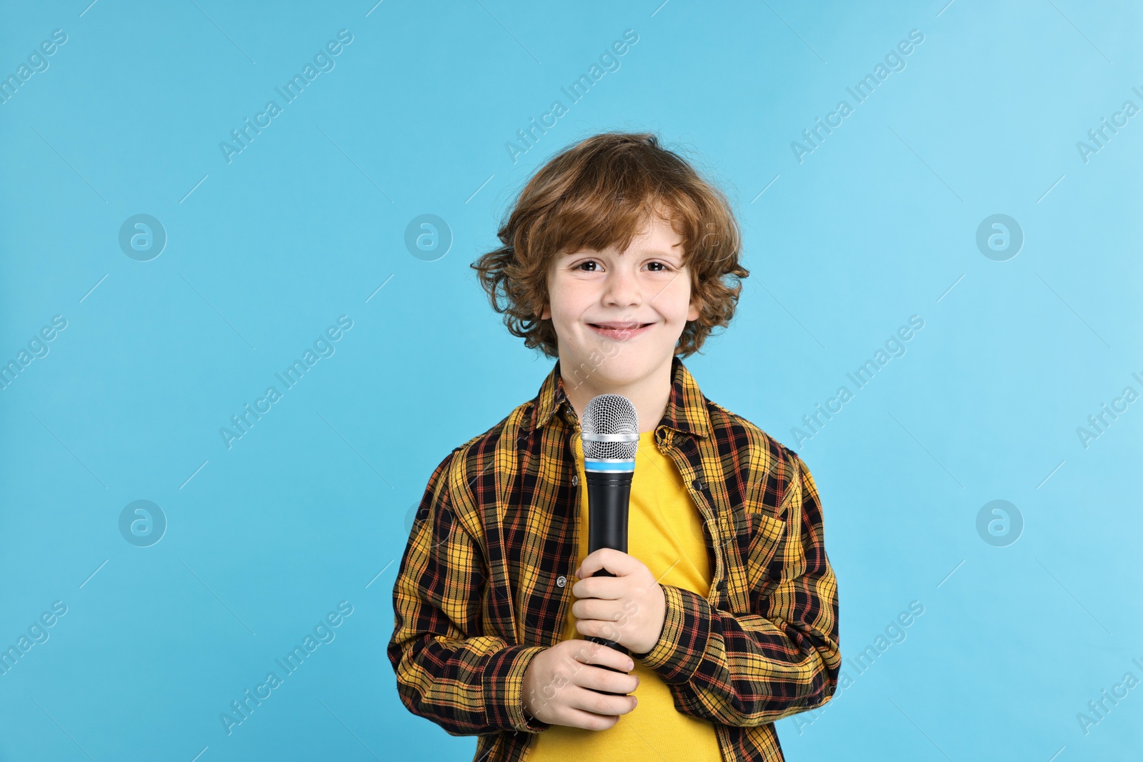 Photo of Little boy with microphone on light blue background, space for text