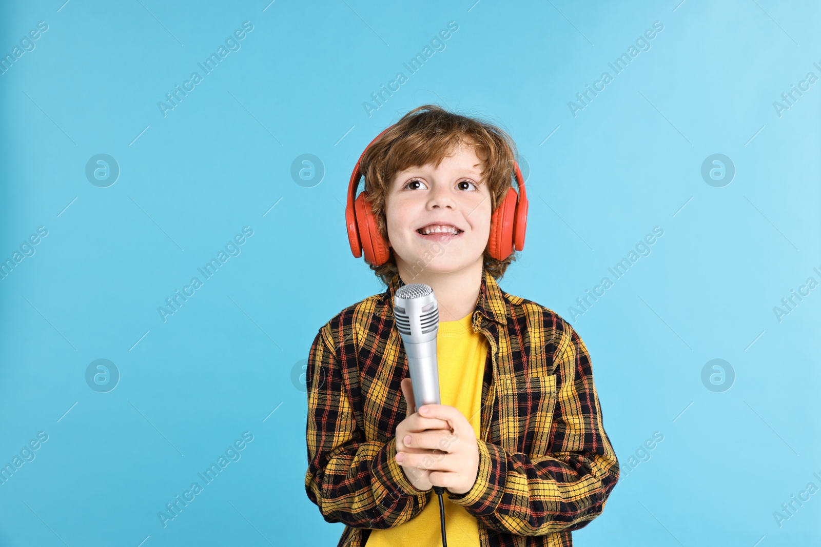 Photo of Little boy with microphone and headphones on light blue background