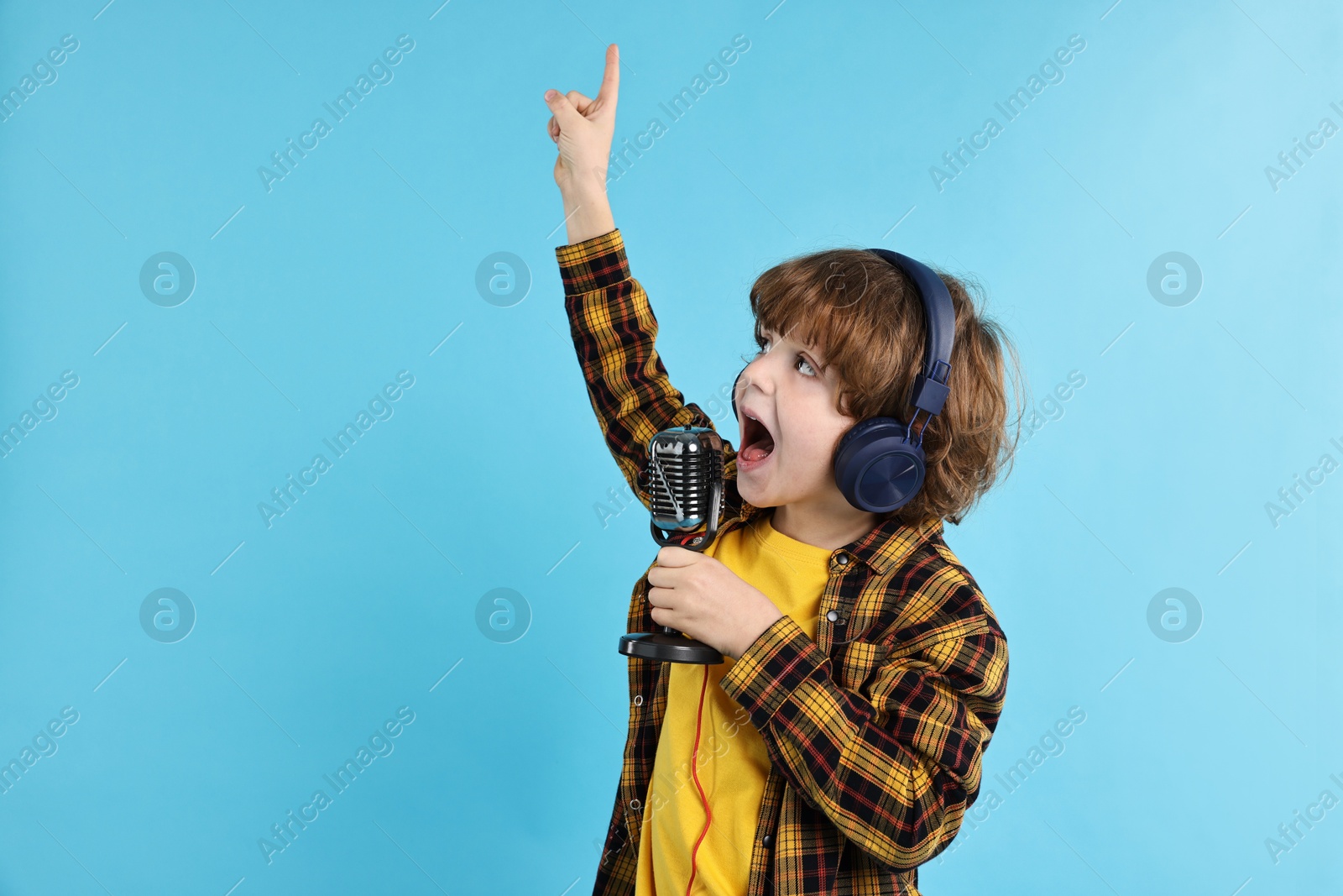 Photo of Little boy with microphone and headphones singing on light blue background, space for text