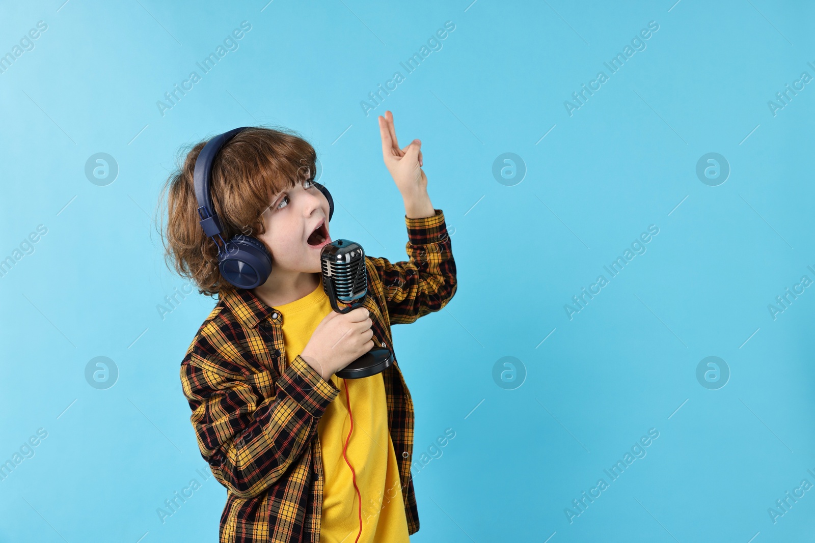 Photo of Little boy with microphone and headphones singing on light blue background, space for text