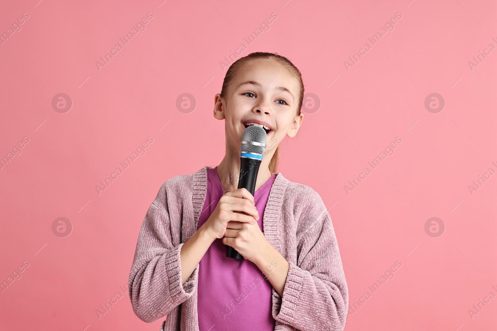 Photo of Little girl with microphone singing on pink background