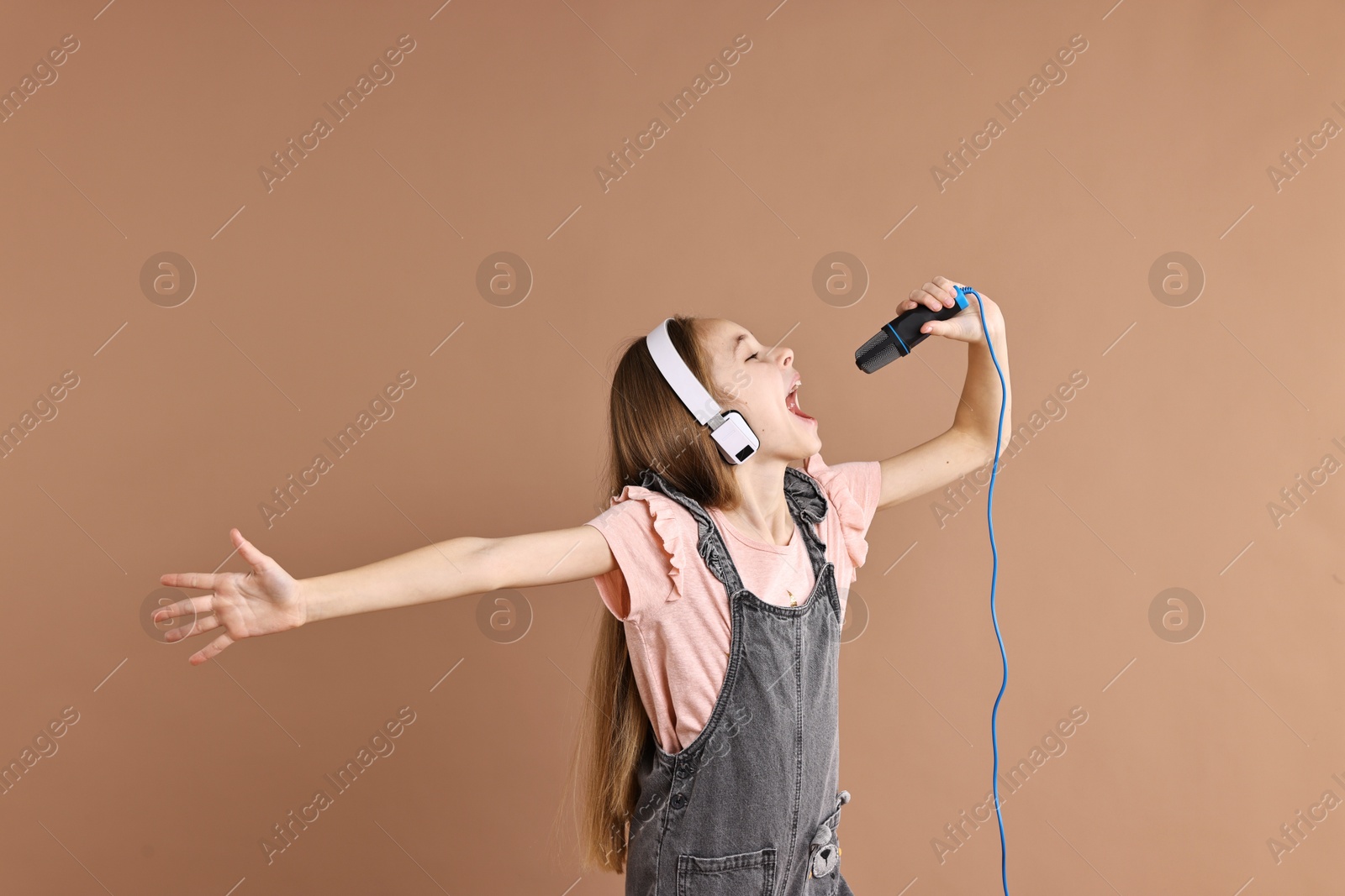 Photo of Little girl with microphone and headphones singing on light brown background