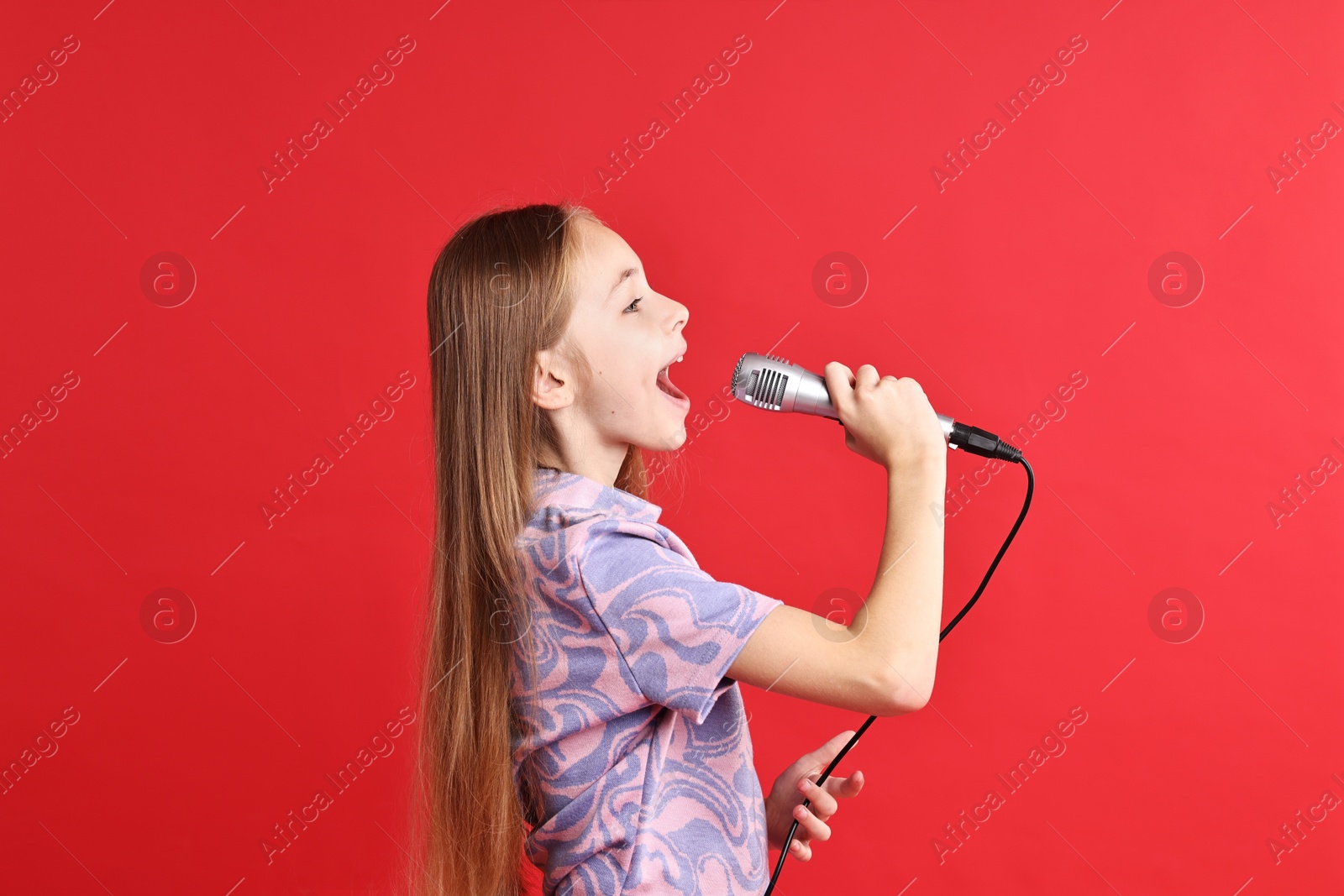 Photo of Little girl with microphone singing on red background