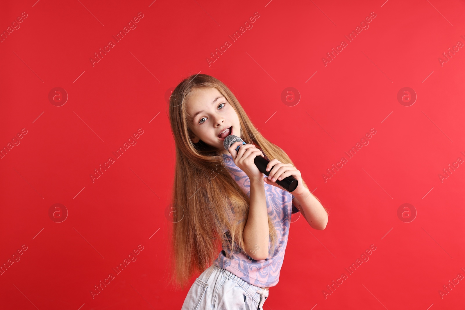 Photo of Little girl with microphone singing on red background