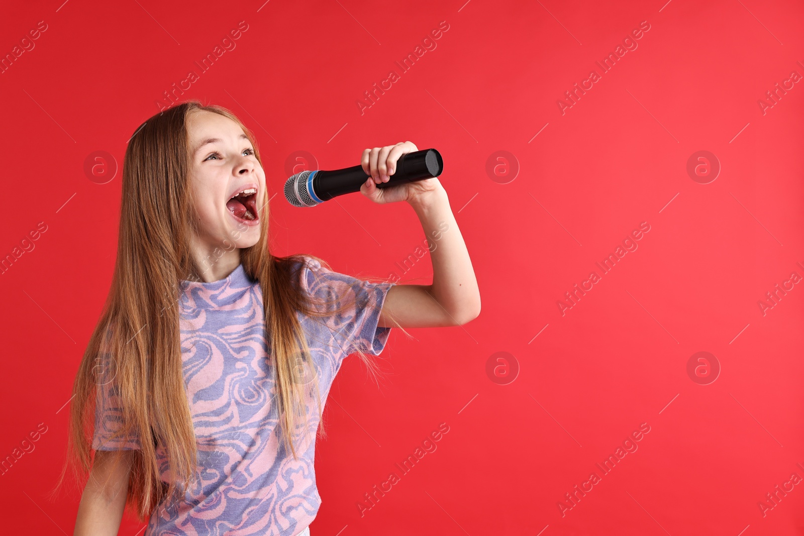 Photo of Little girl with microphone singing on red background, space for text