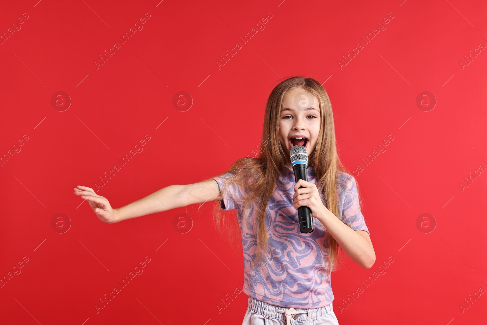 Photo of Little girl with microphone singing on red background