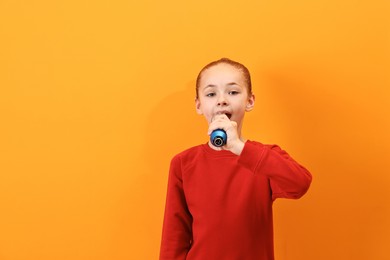 Photo of Little girl with microphone singing on orange background, space for text