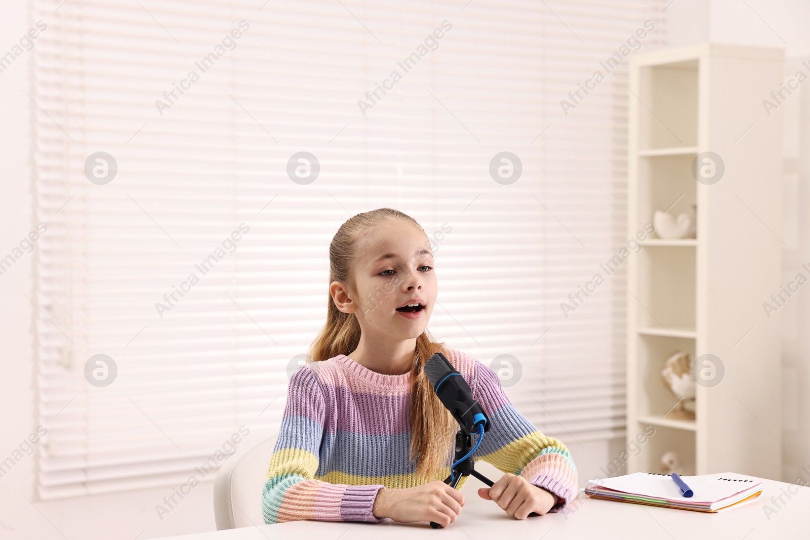 Photo of Little girl with microphone at white table indoors