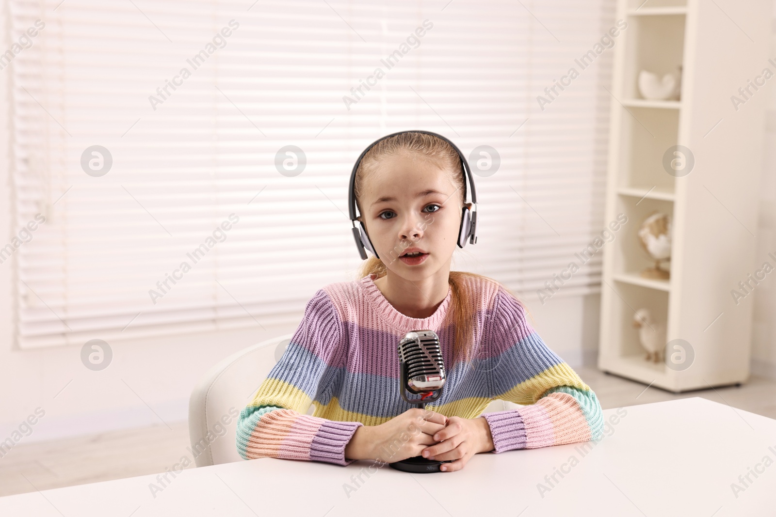 Photo of Little girl with microphone and headphones at white table indoors