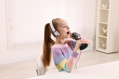 Photo of Little girl with microphone and headphones at white table indoors