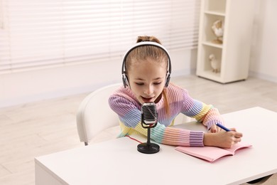 Photo of Little girl with microphone and headphones at white table indoors