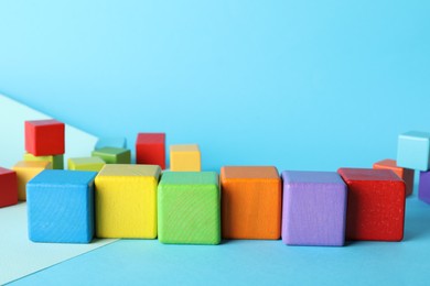 Photo of Colorful wooden cubes on light blue background, space for text