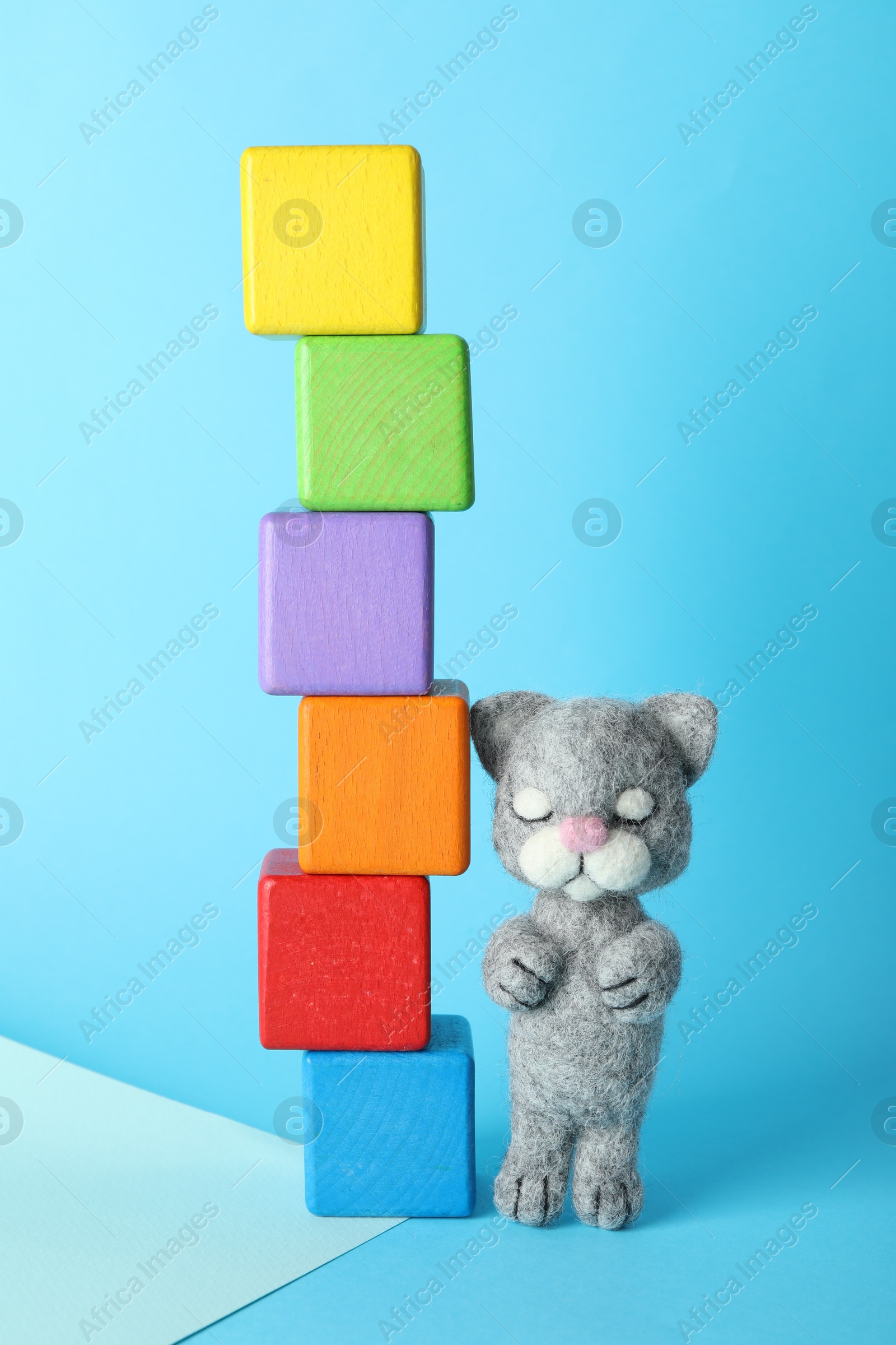 Photo of Colorful wooden cubes and needle felted cat on light blue background