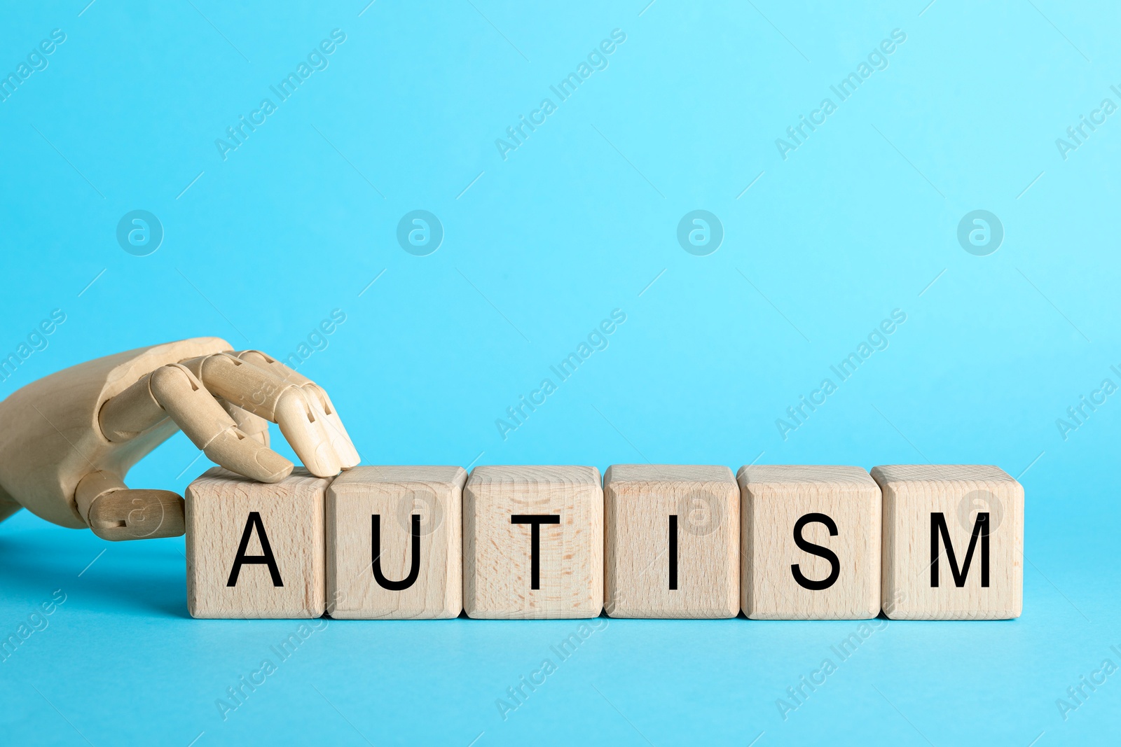 Photo of Word Autism made of wooden cubes and mannequin hand on light blue background, space for text