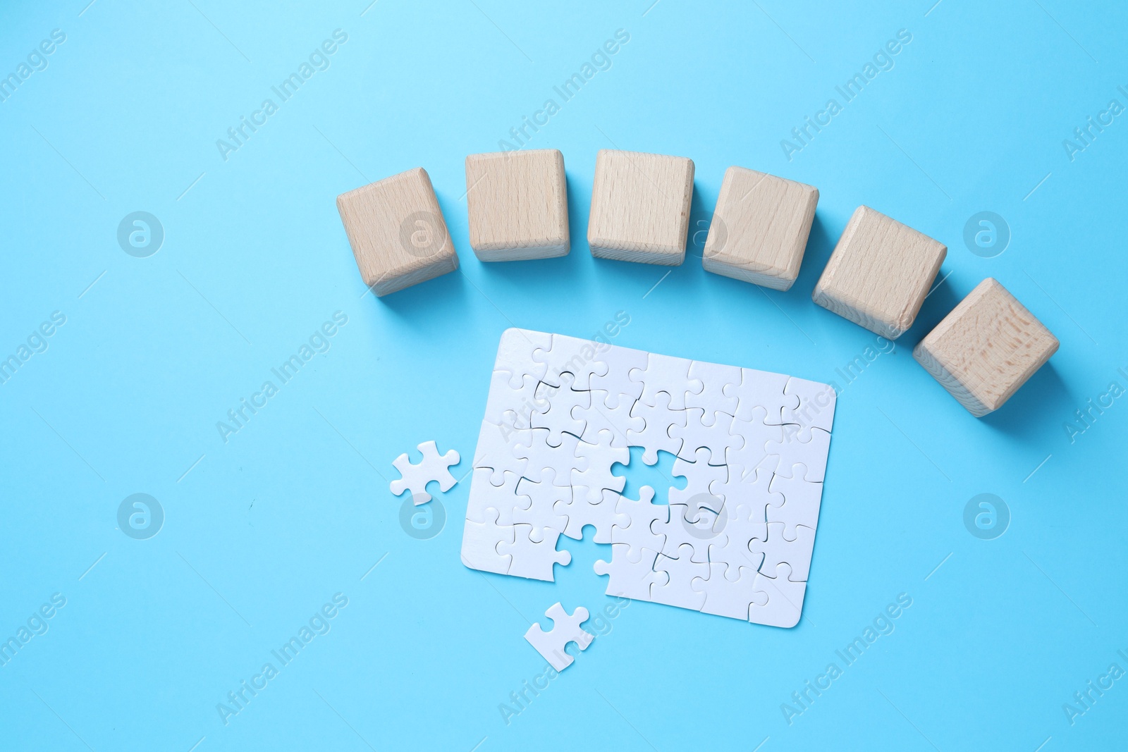 Photo of Wooden cubes and puzzle on light blue background, flat lay. Space for text