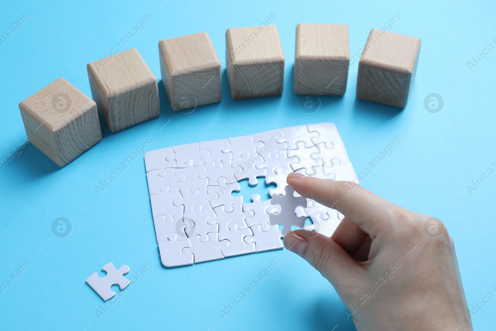 Photo of Woman with puzzle and wooden cubes on light background, closeup