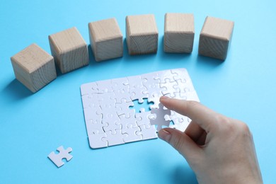 Photo of Woman with puzzle and wooden cubes on light background, closeup