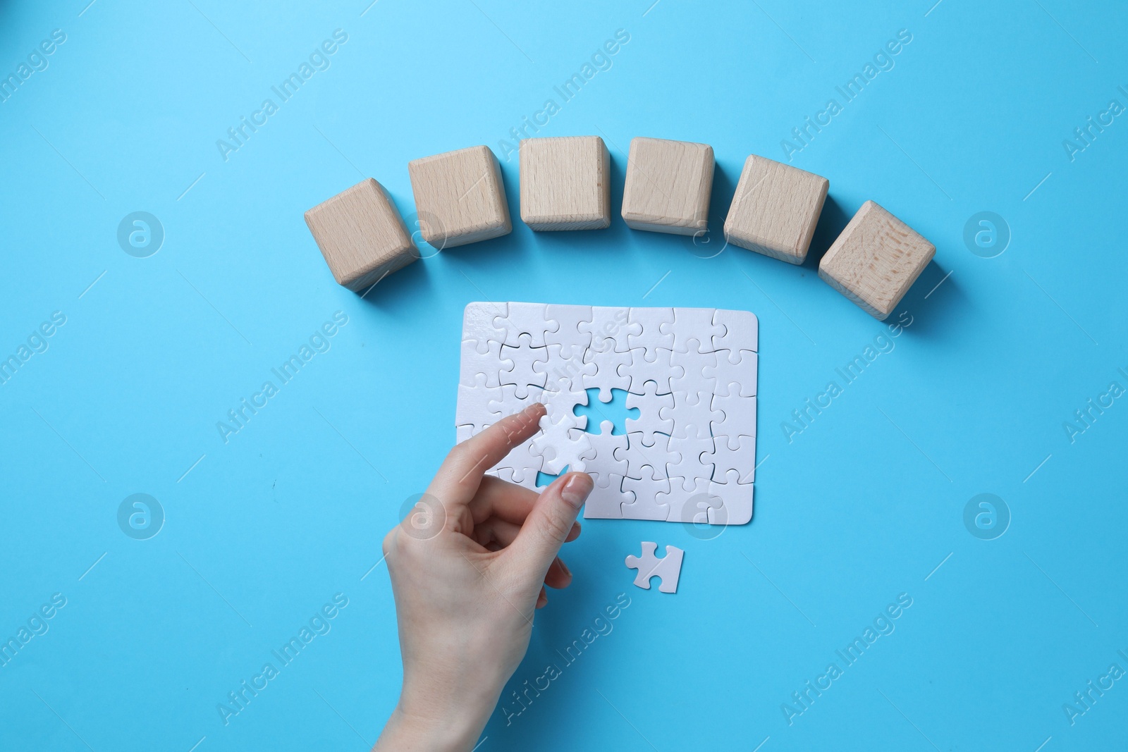 Photo of Woman with puzzle and wooden cubes on light background, top view