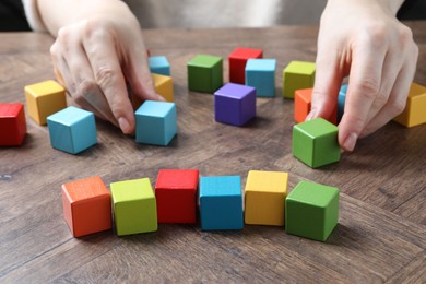 Photo of Woman with colorful cubes at wooden table, closeup