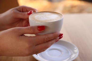 Photo of Woman with cup of aromatic coffee at table in cafe, closeup