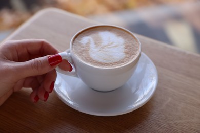 Photo of Woman with cup of aromatic coffee at wooden table in cafe, closeup