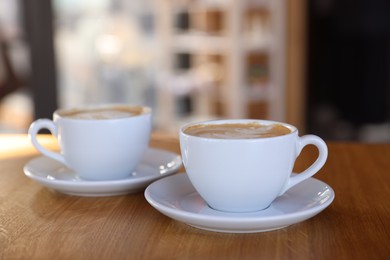 Photo of Cups of aromatic coffee on wooden table in cafe, closeup