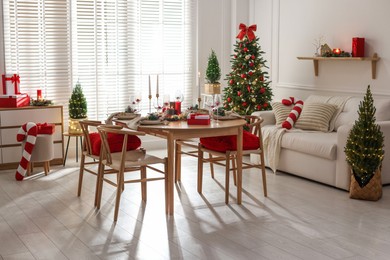 Photo of Christmas table setting with stylish dishware, glasses and burning candles in festive decorated room