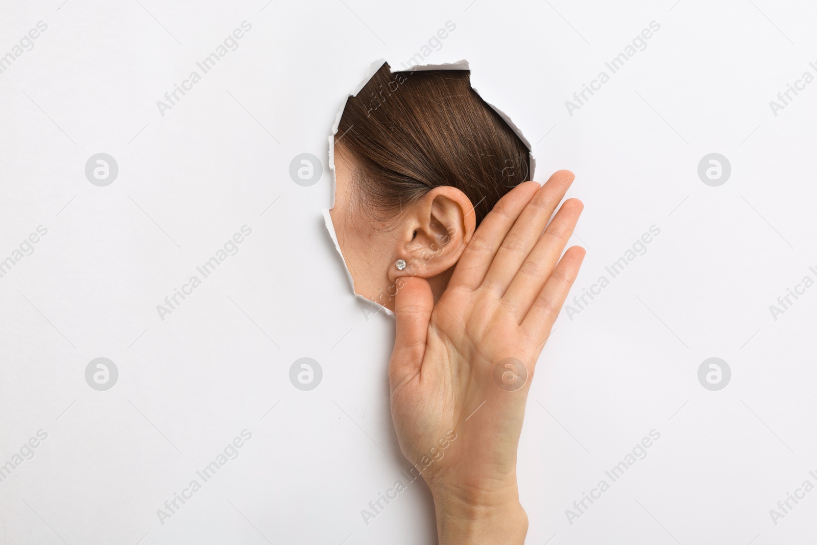 Photo of Woman showing hand to ear gesture through hole in white paper, closeup