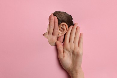 Photo of Woman showing hand to ear gesture through hole in pink paper, closeup