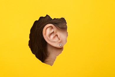 Woman showing her ear through hole in yellow paper, closeup