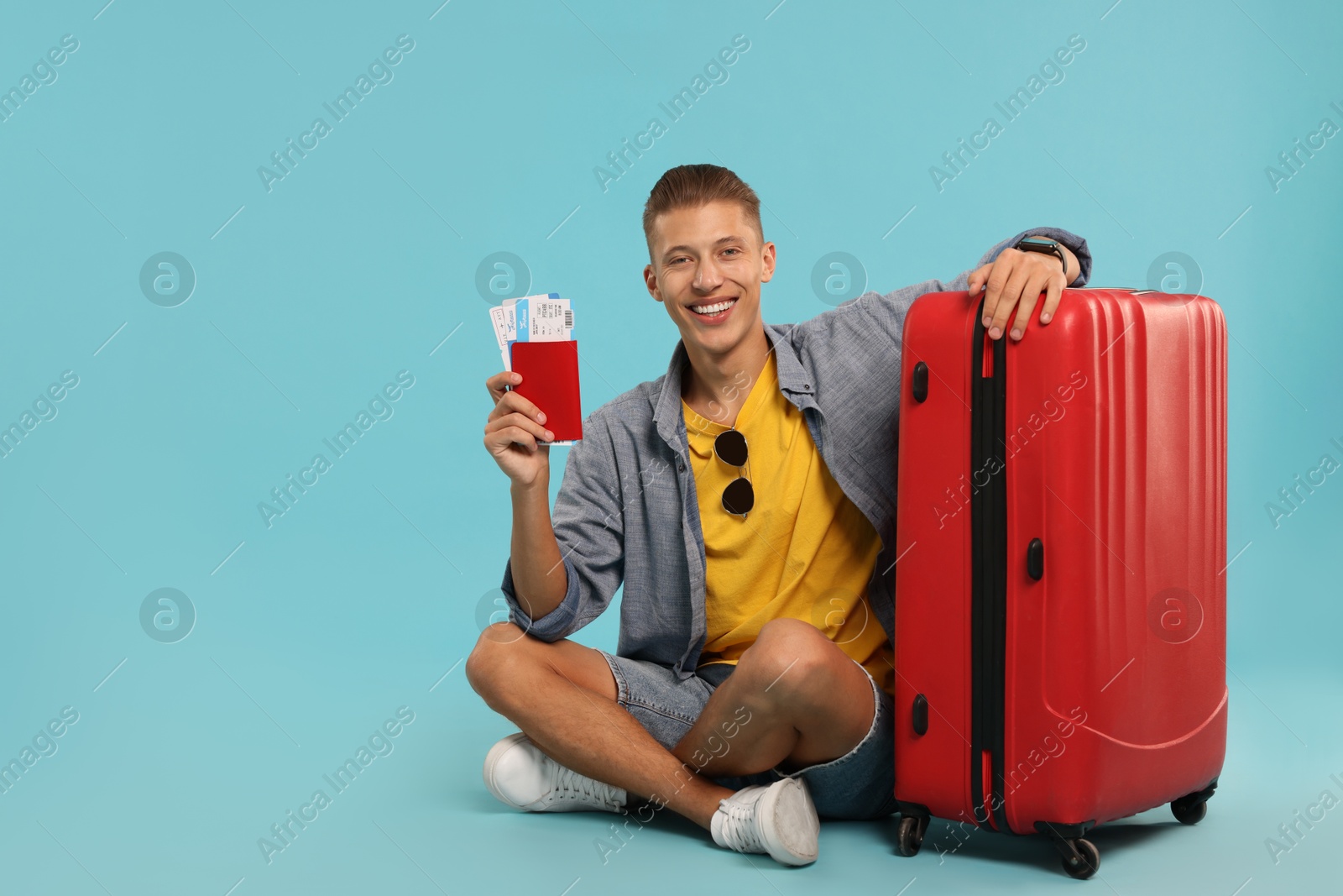 Photo of Happy traveller with suitcase, passport and tickets on light blue background, space for text